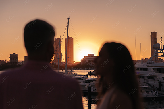 Silhouetted Couple Overlooking Marina at Sunset With Boats and City Skyline