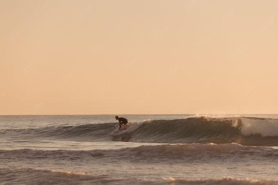 Surfer Riding Small Wave at Sunset With Calm Ocean Horizon