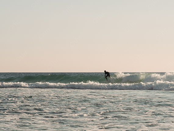 Surfer Riding Small Wave on Calm Ocean Under Soft Daylight